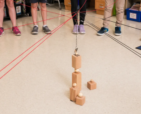 Schulkinder steuern im Klassenzimmer gemeinsam ein Kugeltower-Kooperationsspiel mit Seilen und Holzbausteinen
